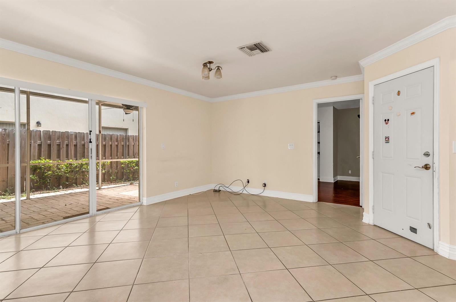An empty living room features beige tile flooring, a sliding glass door, and a white door — 5486 NW 44th Way, Coconut Creek FL 33073, COCONUT CREEK, FL