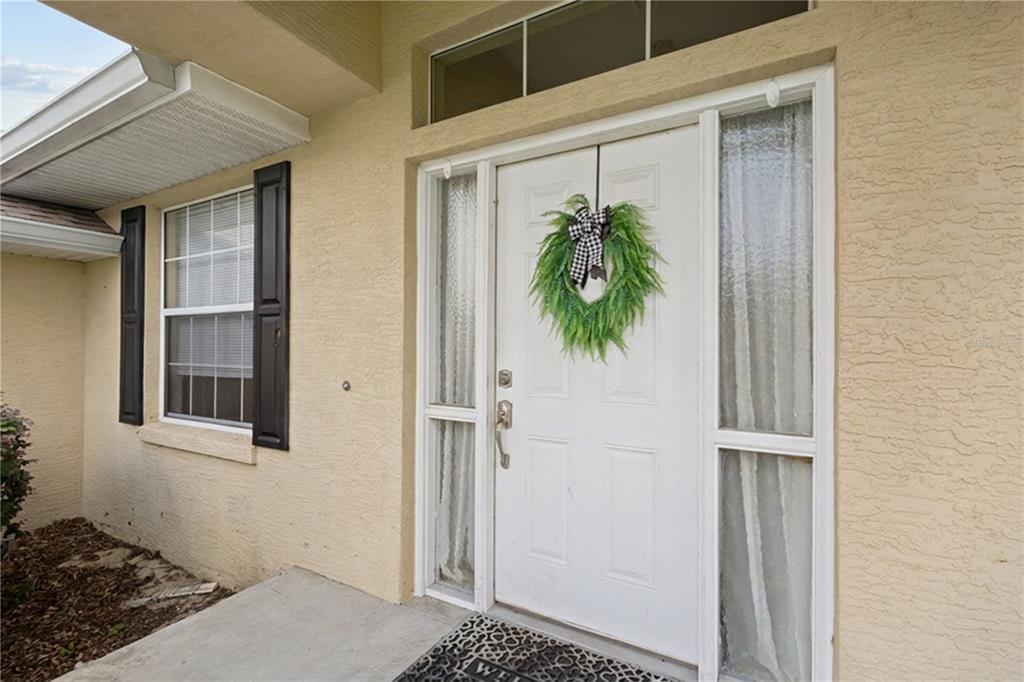 A white front door with a green wreath and sidelights on a beige house exterior — 5320 SW 115TH LOOP, OCALA, FL