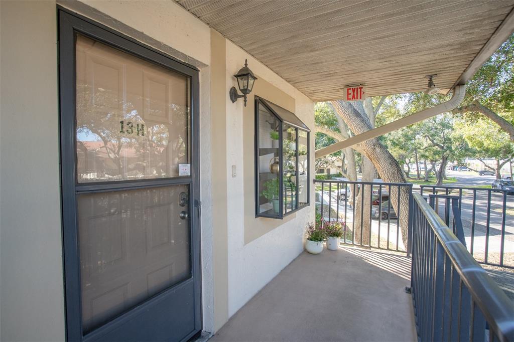 An exterior view of a covered apartment balcony with a door labeled 13H — 11511 113TH STREET UNIT 13H, LARGO, FL
