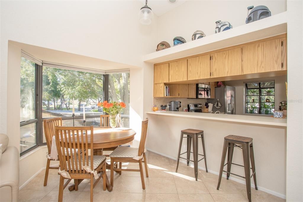 A dining area with a bay window, wooden table, and breakfast bar with two stools — 11511 113TH STREET UNIT 13H, LARGO, FL