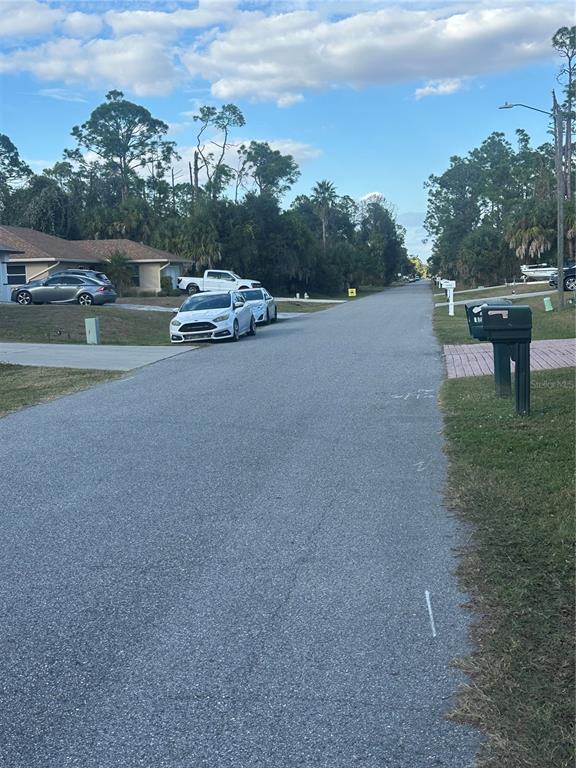 A residential street with parked cars, mailboxes, and houses surrounded by trees under a blue sky — ALIBI TERRACE, NORTH PORT, FL