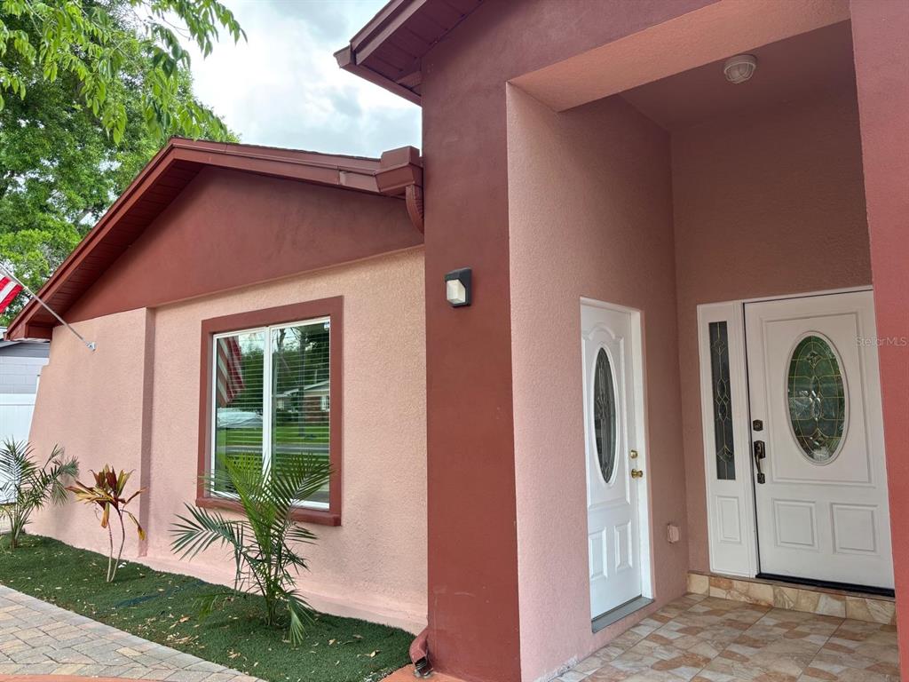 A stucco house exterior features a red-trimmed window, a white front door, and a covered entryway — 6747 RALSTON BEACH CIRCLE, TAMPA, FL
