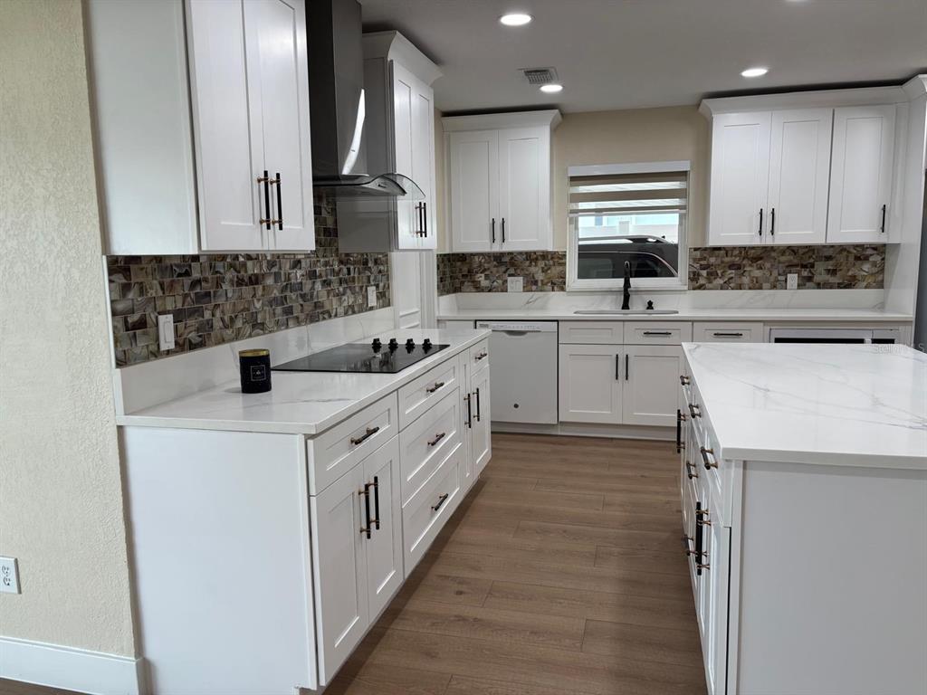 A modern kitchen features white cabinets, a marble-look island, and a mosaic tile backsplash — 6747 RALSTON BEACH CIRCLE, TAMPA, FL