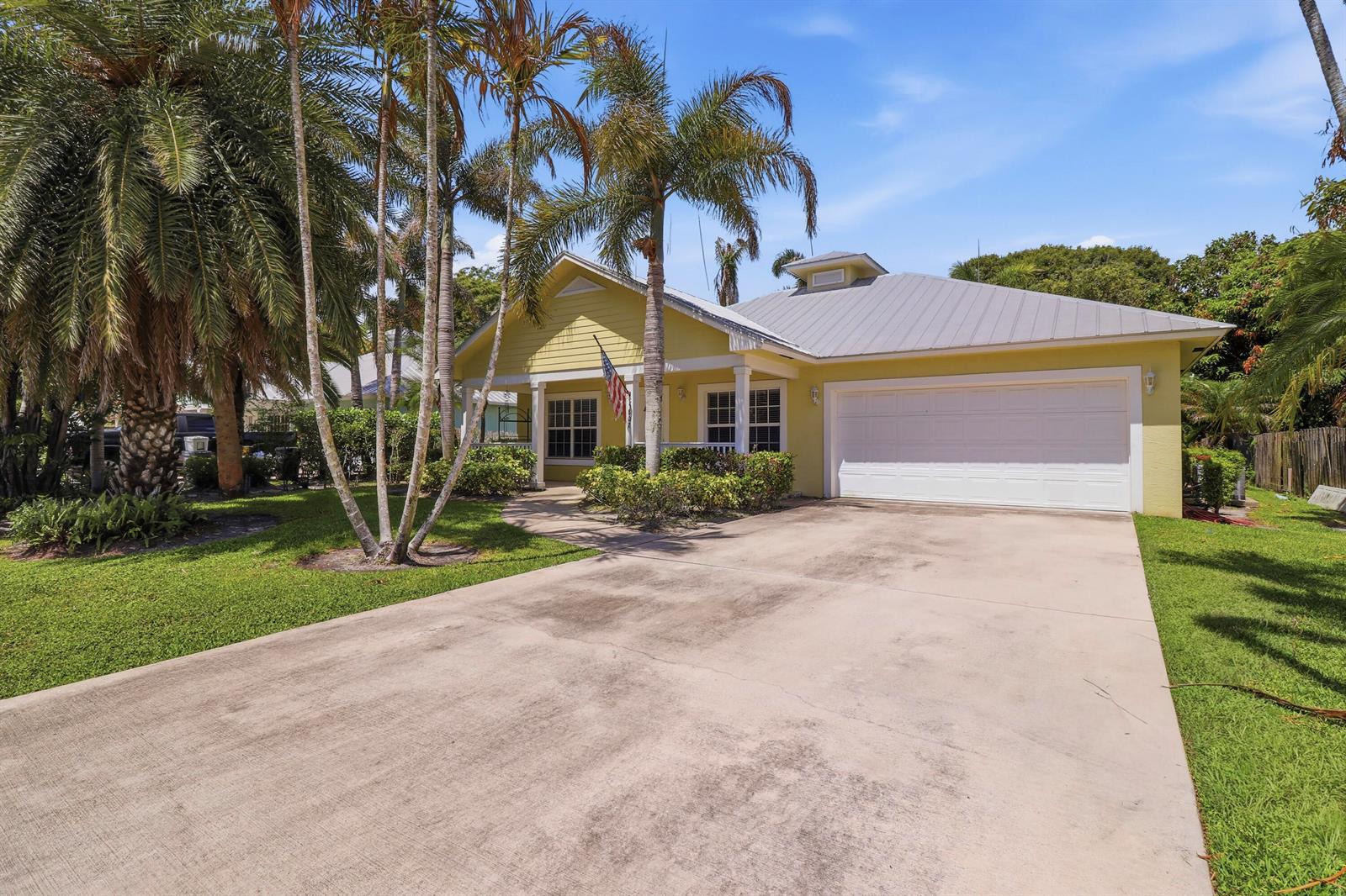 A yellow single-story house with a metal roof, two-car garage, and palm trees in front — 5802 SE Wesley Avenue, Stuart FL 34997, STUART, FL