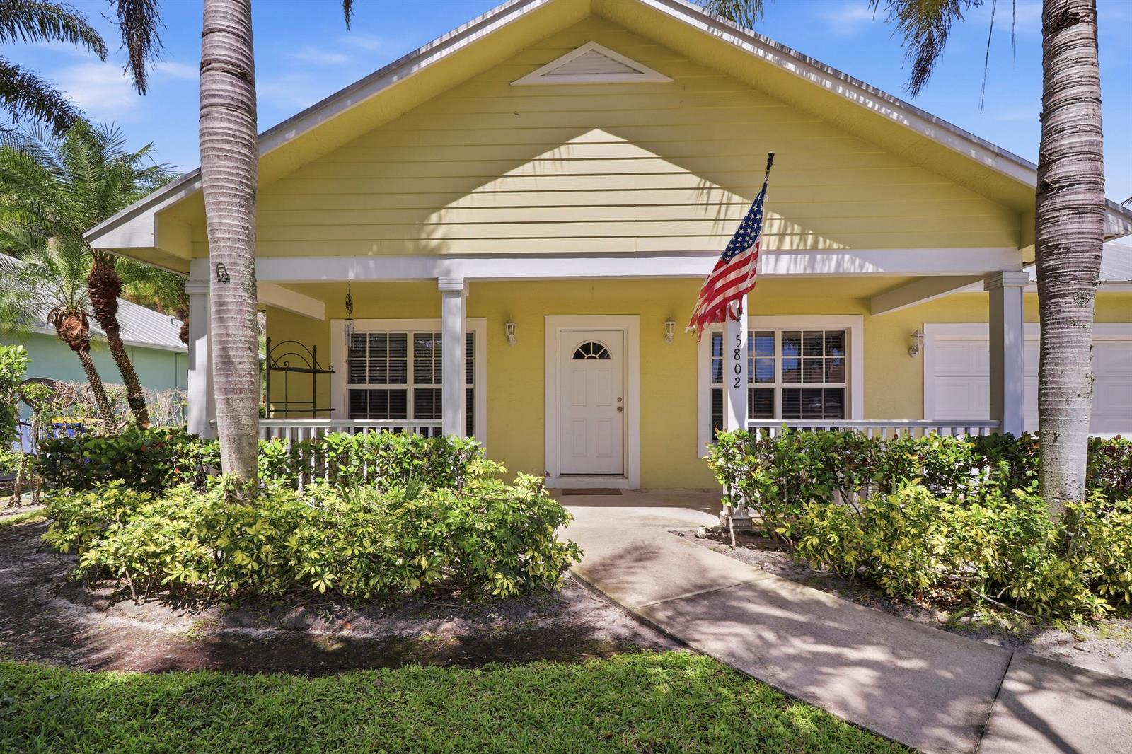 A yellow house with a front porch, palm trees, and an American flag — 5802 SE Wesley Avenue, Stuart FL 34997, STUART, FL