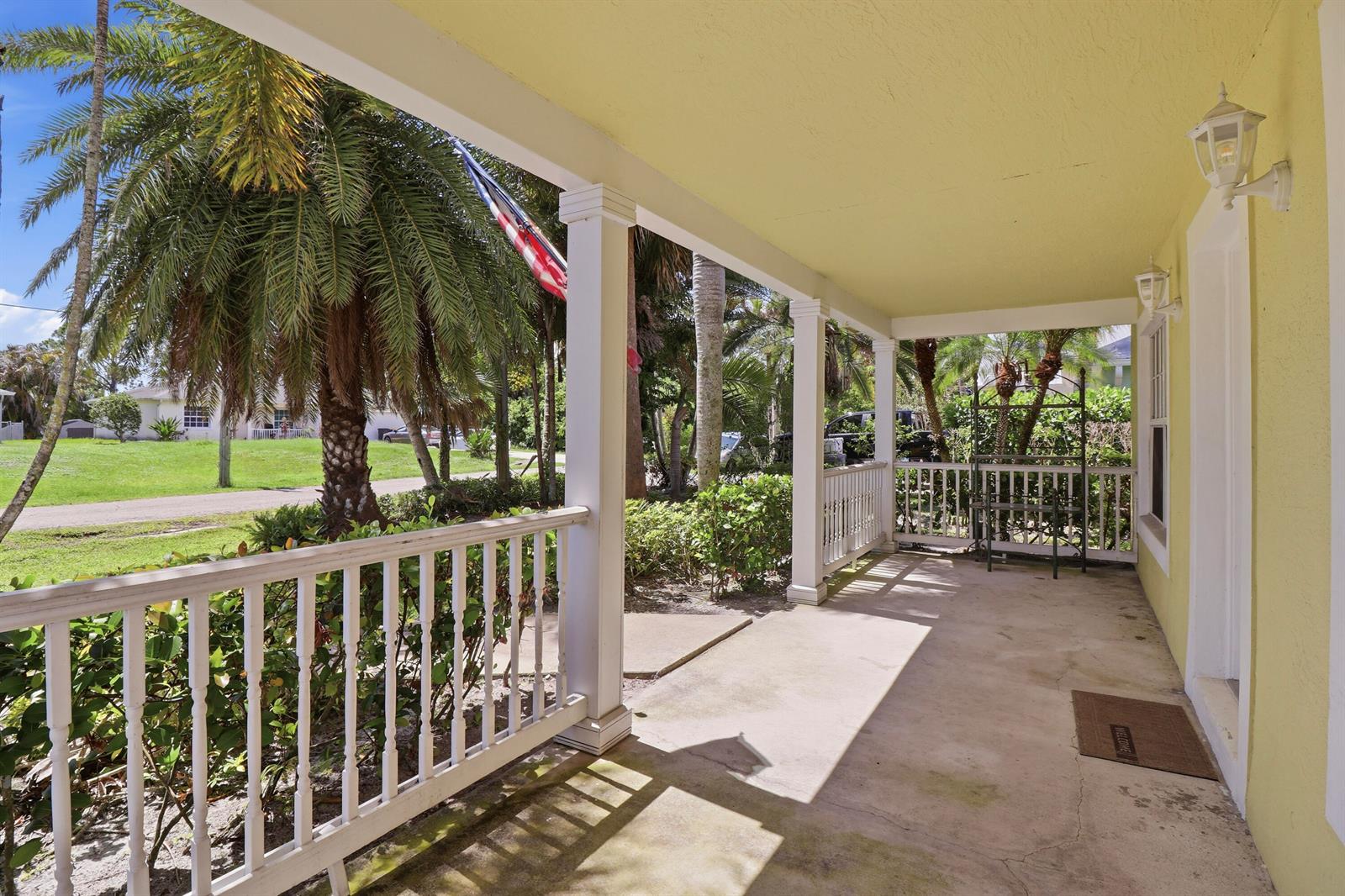 A covered front porch with white railings, yellow walls, and a concrete floor — 5802 SE Wesley Avenue, Stuart FL 34997, STUART, FL