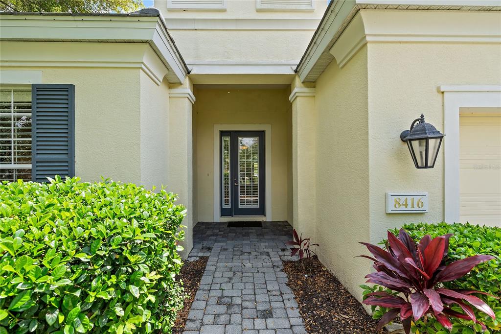 A paved walkway leads to the front entrance of a house with light-colored stucco walls — 8416 ABINGDON COURT, UNIVERSITY PARK, FL