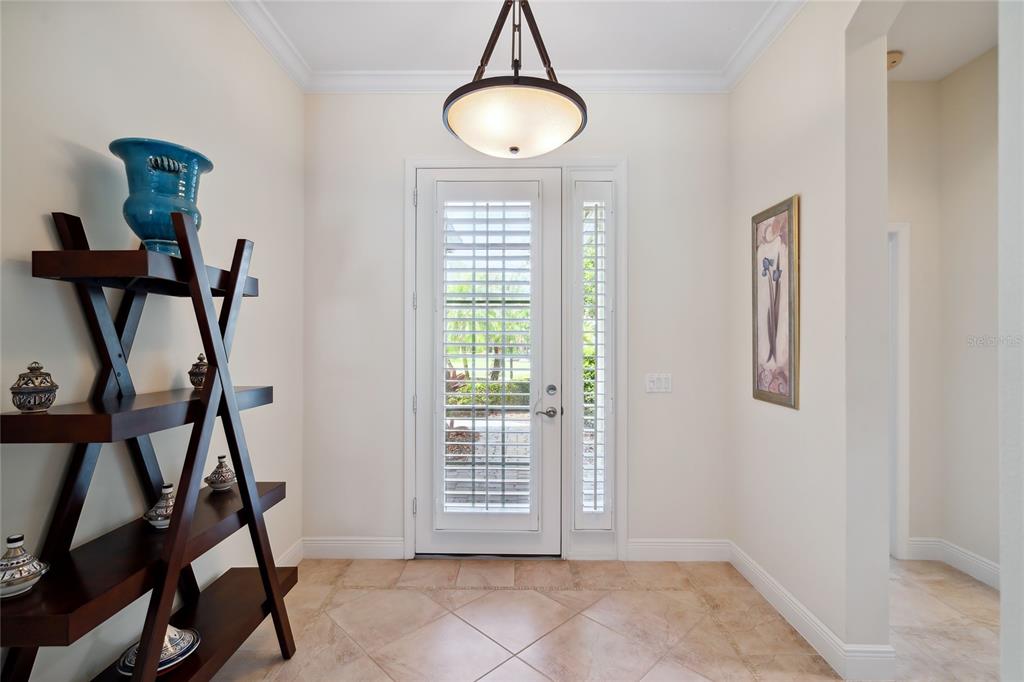A bright entryway features a tile floor, a wooden display shelf, and a glass-paneled door — 8416 ABINGDON COURT, UNIVERSITY PARK, FL