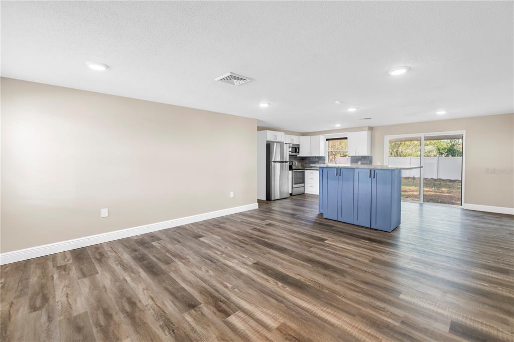 An empty living room features light beige walls, wood-look flooring, a window, and recessed lighting — 518 62ND AVENUE NE, ST PETERSBURG, FL