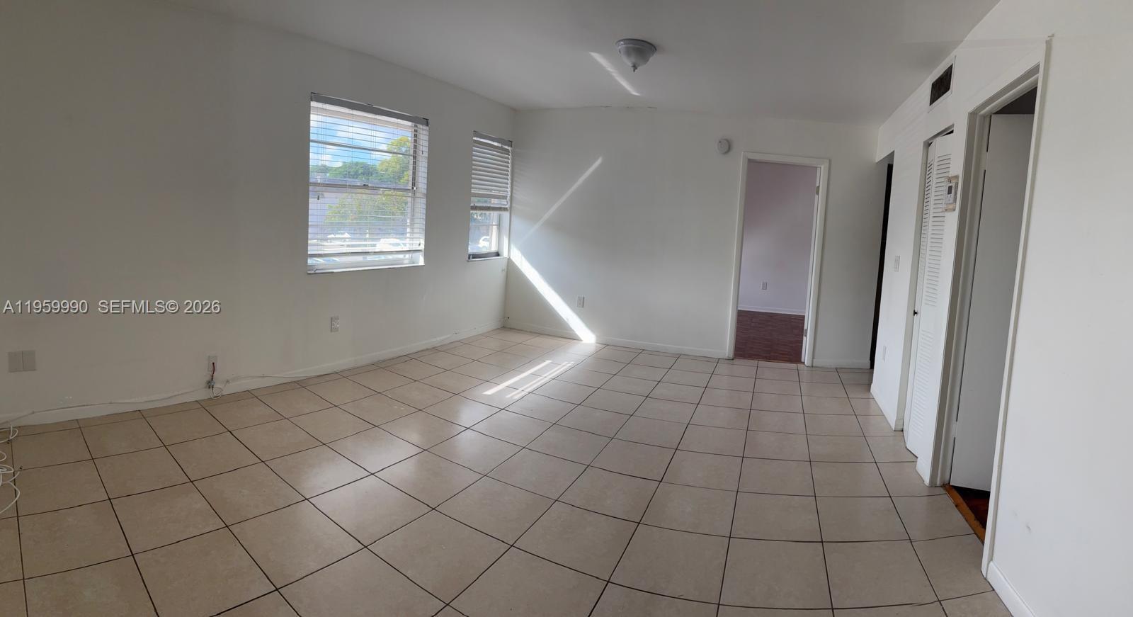 An empty room features white walls, light-colored tile flooring, two windows, and two doorways — 6911 SW 129 AV # 5, Miami FL 33183, MIAMI, FL