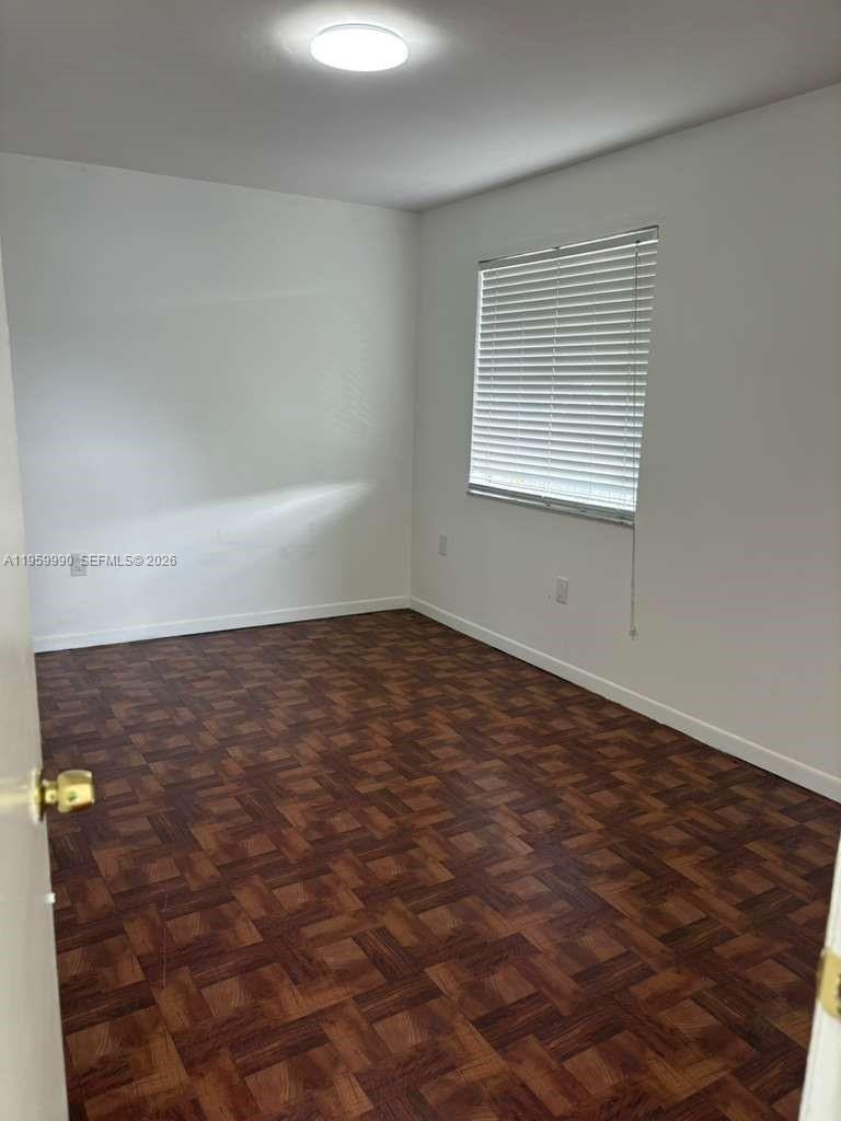 An empty bedroom features white walls, a window with blinds, and dark parquet flooring — 6911 SW 129 AV # 5, Miami FL 33183, MIAMI, FL