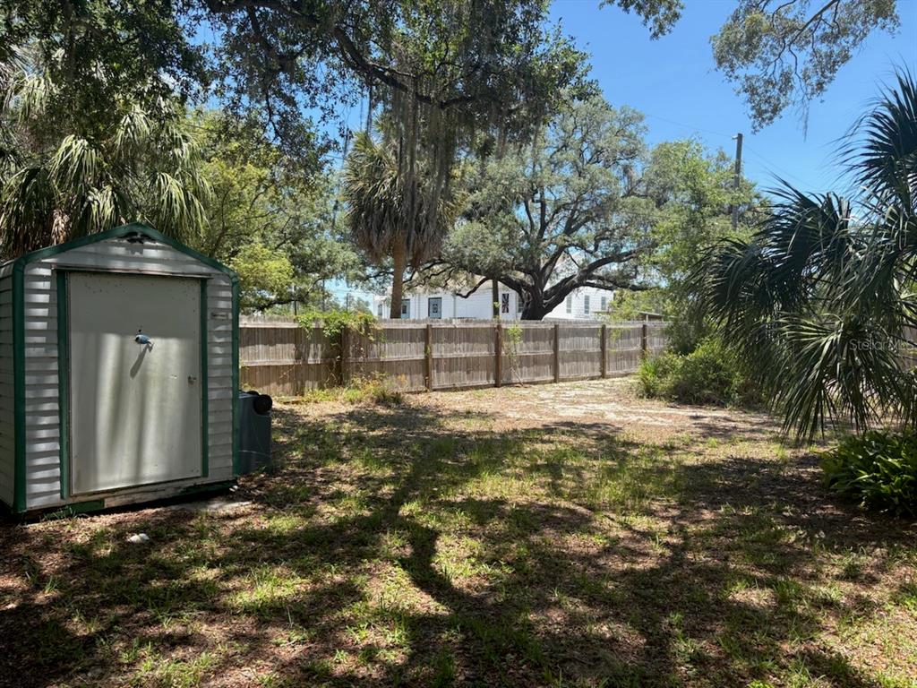 A backyard features a small storage shed, a wooden fence, and mature trees — 439 E MARTIN LUTHER KING JR DRIVE, TARPON SPRINGS, FL