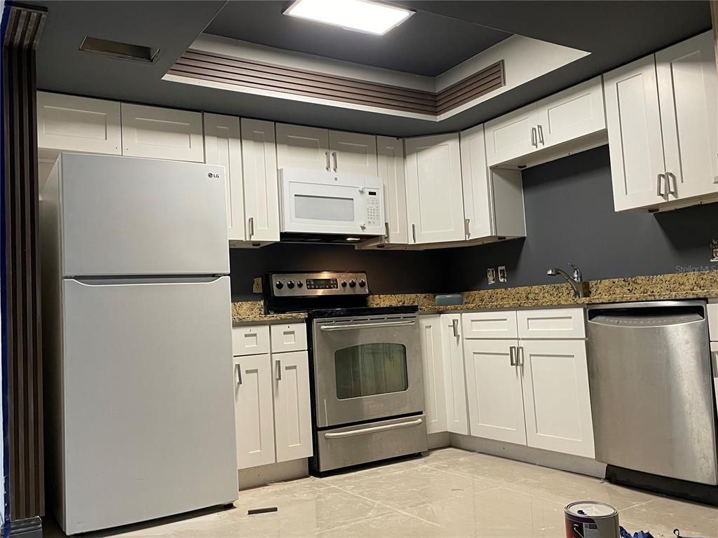 A kitchen features white cabinets, stainless steel appliances, granite countertops, and dark gray walls — 7352 BALBOA DRIVE UNIT 7352, ORLANDO, FL
