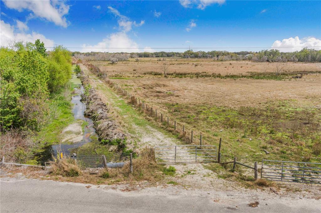 A dirt path leads through a metal gate into a large, open, grassy field — 3705 HIGH STREET, WINTER HAVEN, FL