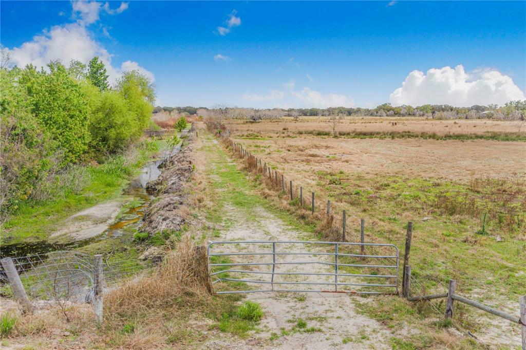 A metal gate opens onto a dirt path between a drainage ditch and a field — 3705 HIGH STREET, WINTER HAVEN, FL