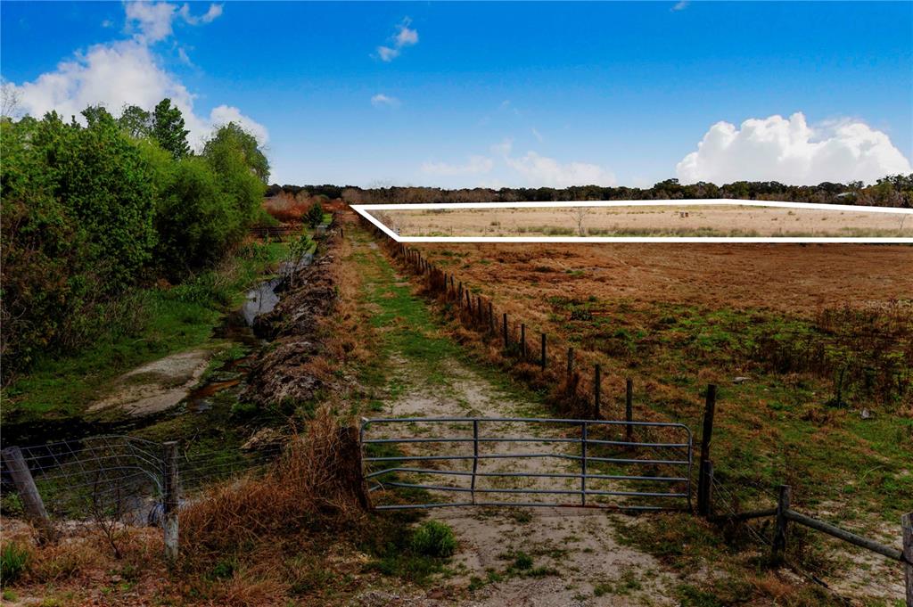 A metal gate opens to a dirt path beside a field and a small creek — 3705 HIGH STREET, WINTER HAVEN, FL