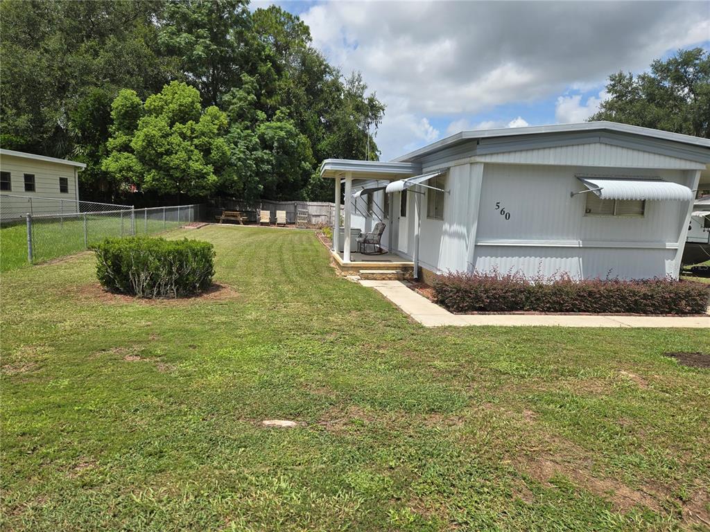 A light-colored mobile home features a covered porch and a spacious, grassy side yard — 560 NE 62ND TERRACE, OCALA, FL