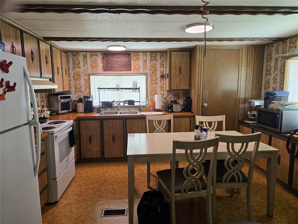 A kitchen features wood-paneled cabinets, floral wallpaper, a dining table, and a white stove — 560 NE 62ND TERRACE, OCALA, FL
