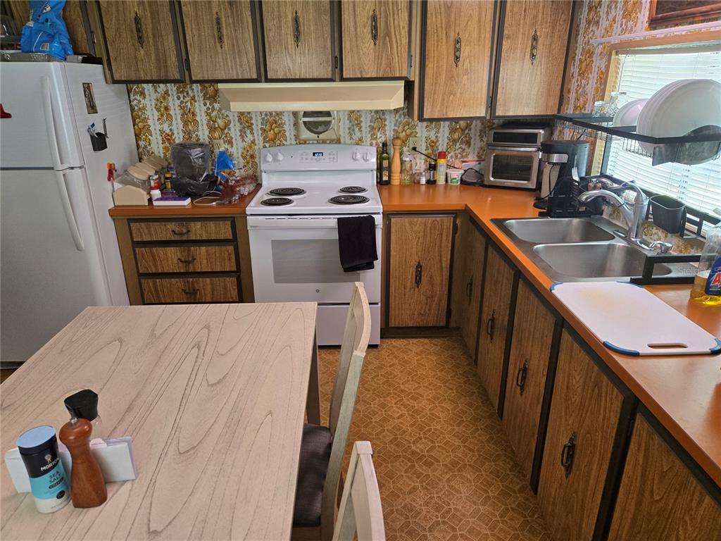 A kitchen features wood-grain cabinets, orange countertops, floral wallpaper, and a white electric stove — 560 NE 62ND TERRACE, OCALA, FL