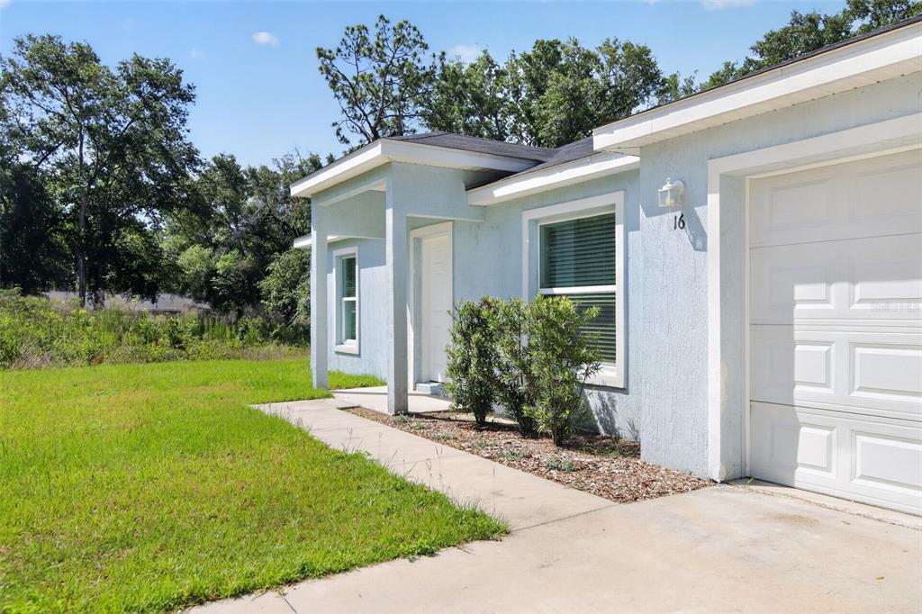 A light blue house exterior features a white garage door, a front entrance, and landscaping — 16 SPRING LOOP COURT, OCALA, FL