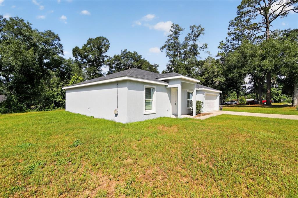 A light-colored, single-story house with a hip roof sits on a large, grassy lot — 16 SPRING LOOP COURT, OCALA, FL