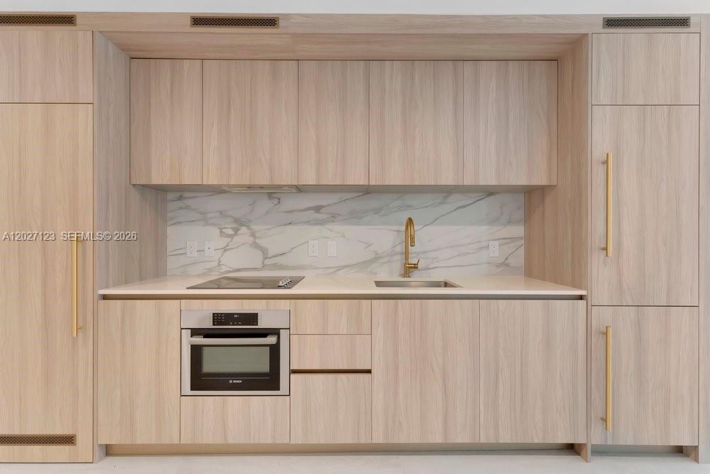 A modern kitchen features light wood cabinetry, a marble backsplash, and integrated stainless steel appliances — 77 SE 5th # 1711, Miami FL 33131, MIAMI, FL