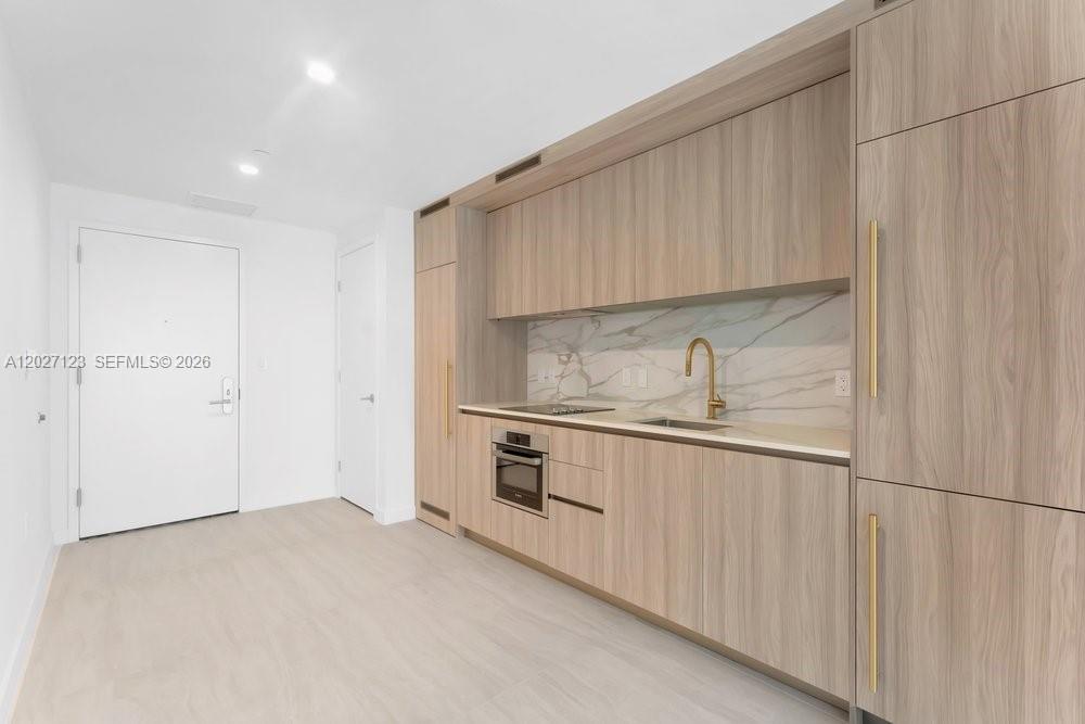 A modern kitchen features light wood cabinetry, a marble backsplash, and integrated appliances — 77 SE 5th # 1711, Miami FL 33131, MIAMI, FL