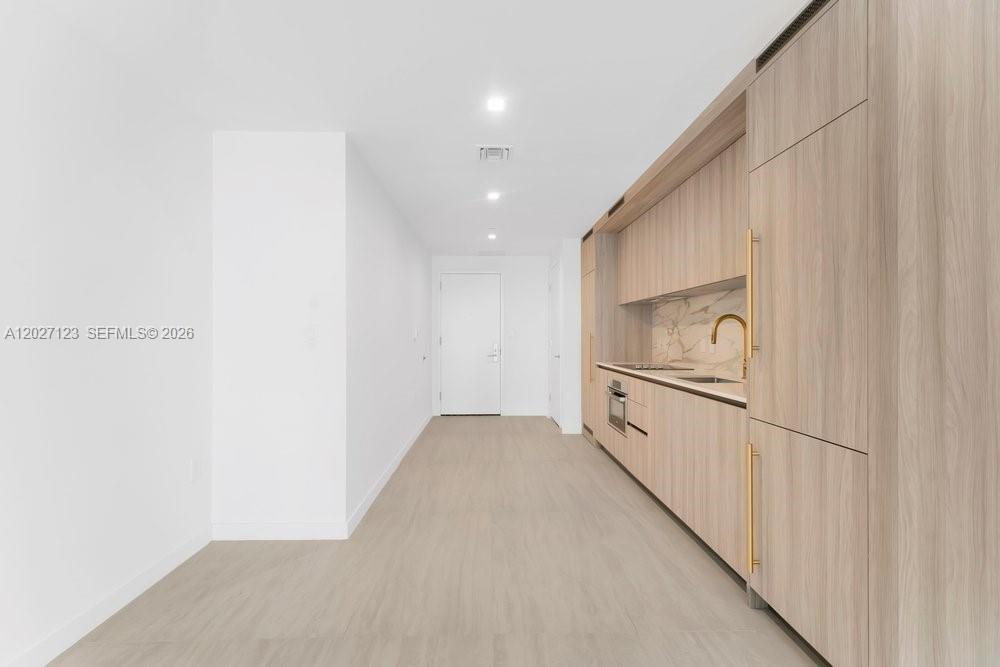 A modern kitchen features light wood cabinetry, gold hardware, and a marble backsplash — 77 SE 5th # 1711, Miami FL 33131, MIAMI, FL