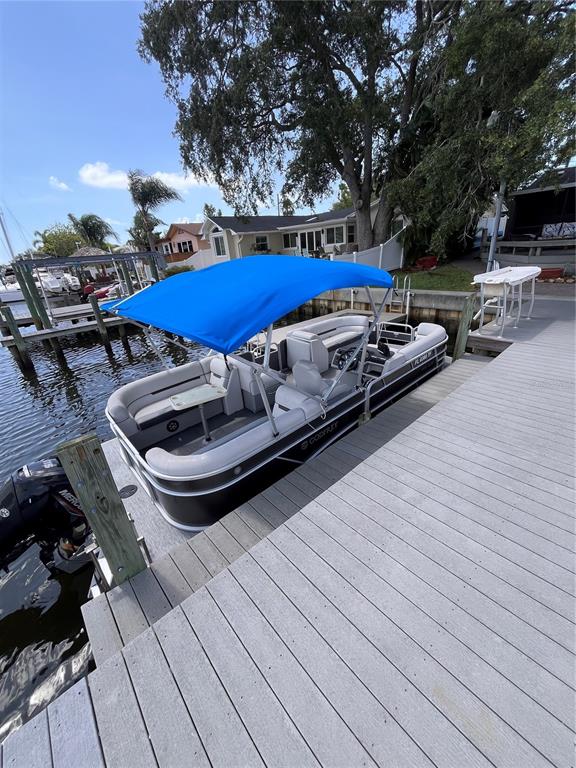 A pontoon boat with a blue canopy is docked at a wooden pier — 378 WESTWINDS DRIVE, PALM HARBOR, FL