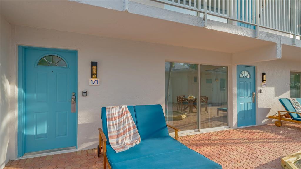 A patio with two blue lounge chairs sits in front of two blue entry doors — 104 AVENIDA VENECCIA UNIT 171, SARASOTA, FL