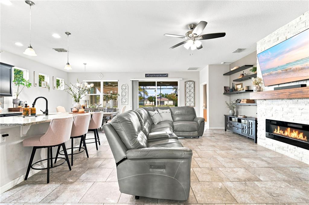 An open-concept living room and kitchen feature a grey sectional, fireplace, and breakfast bar — 632 E VICTORIA TRAILS BOULEVARD, DELAND, FL
