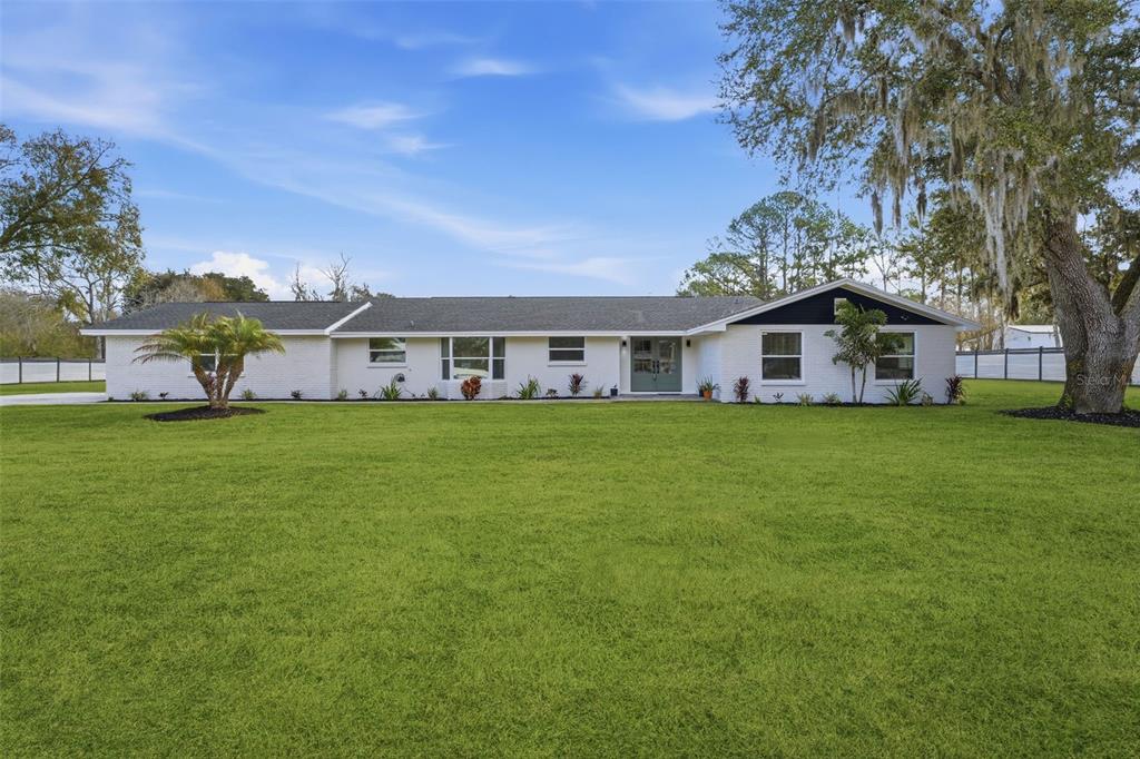 A single-story white brick house with a dark roof sits on a large grassy lawn — 2338 MEADOWBROOK DRIVE, LUTZ, FL