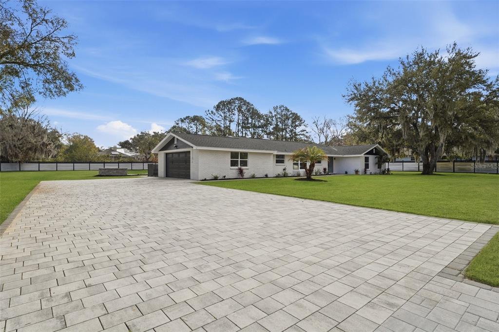 A single-story white brick house with a paved driveway and a large green lawn — 2338 MEADOWBROOK DRIVE, LUTZ, FL