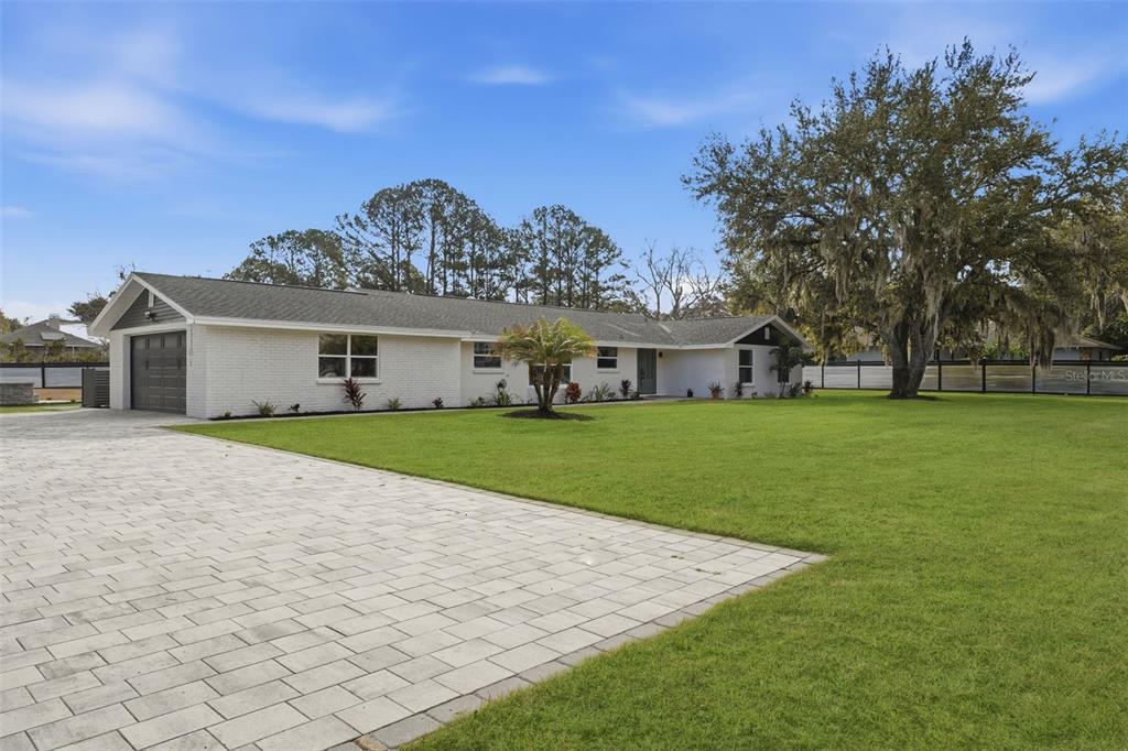 A single-story white brick house with a paved driveway and a large front lawn — 2338 MEADOWBROOK DRIVE, LUTZ, FL