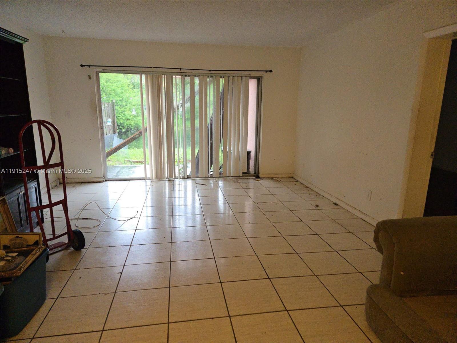 An empty room features white tiled floors, a sliding glass door, and a red dolly — 1524 NW 56th Ave # 7, Lauderhill FL 33313, LAUDERHILL, FL