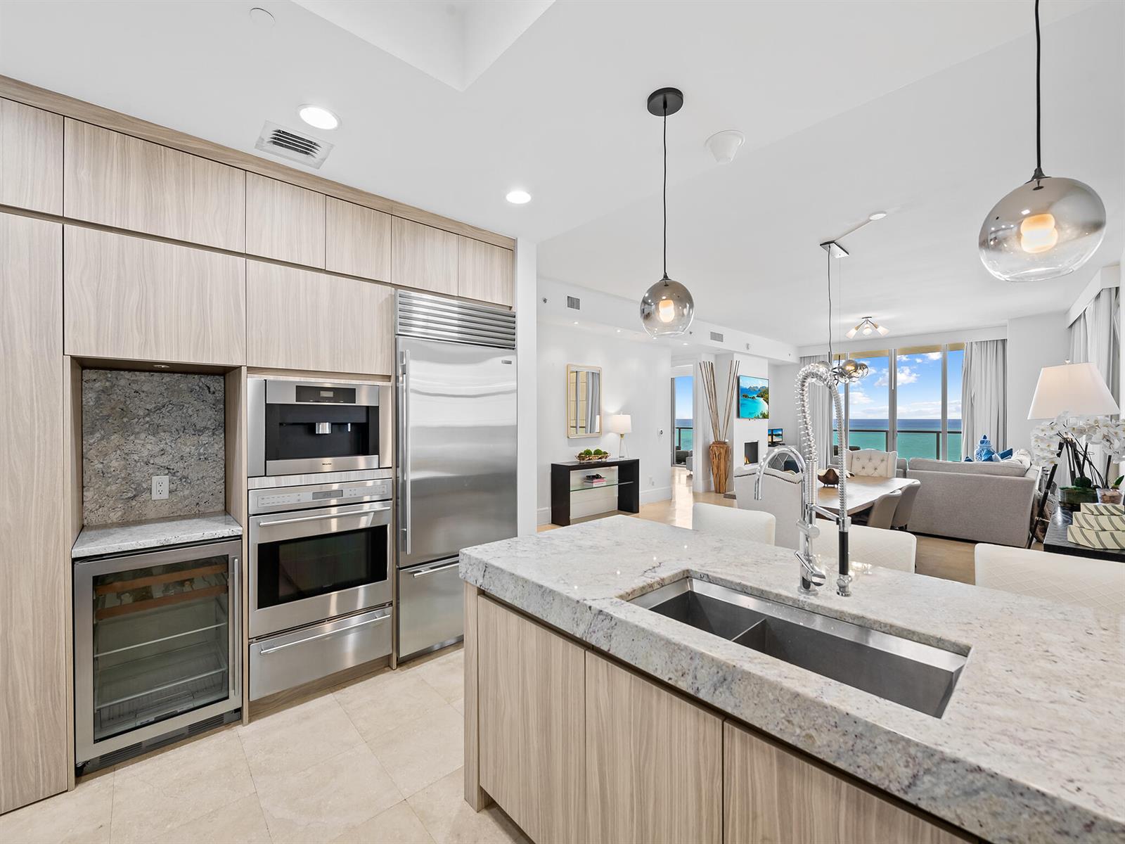 A modern kitchen features light wood cabinetry, stainless steel appliances, and a granite-topped island — 9705 Collins Avenue # 1104n, Bal Harbour FL 33154, BAL HARBOUR, FL