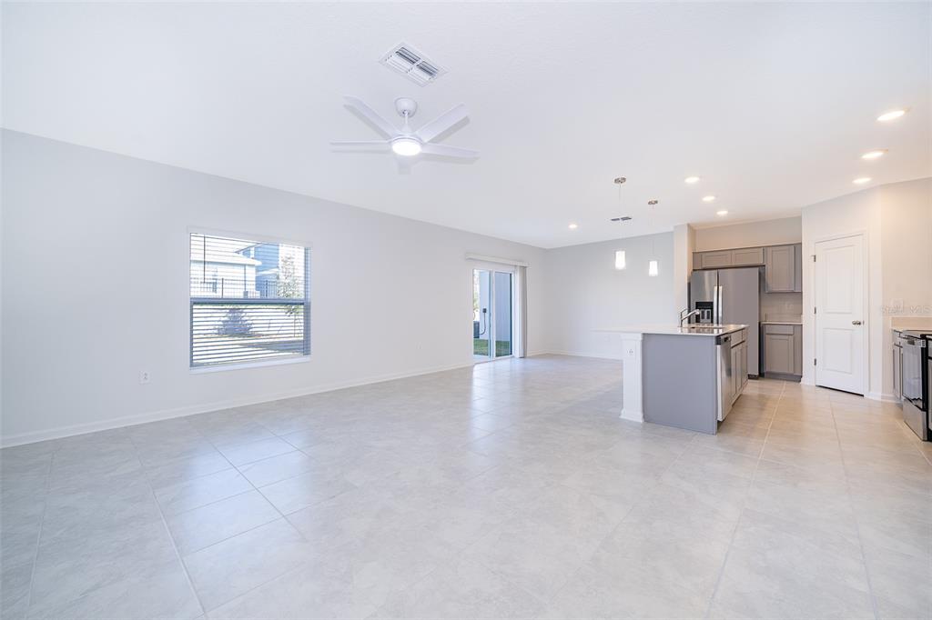 A bright, open-concept living area features light tile flooring, a ceiling fan, and a kitchen — 2723 GENTLE RAIN DRIVE, DAVENPORT, FL