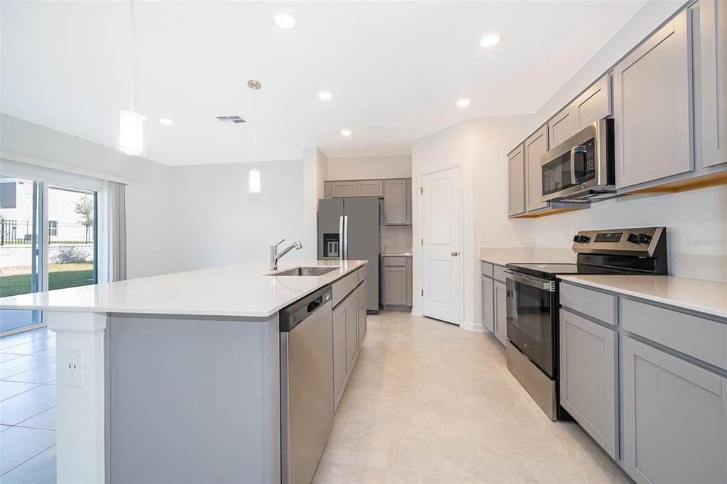 A kitchen features gray cabinets, stainless steel appliances, a white island, and tile flooring — 2723 GENTLE RAIN DRIVE, DAVENPORT, FL