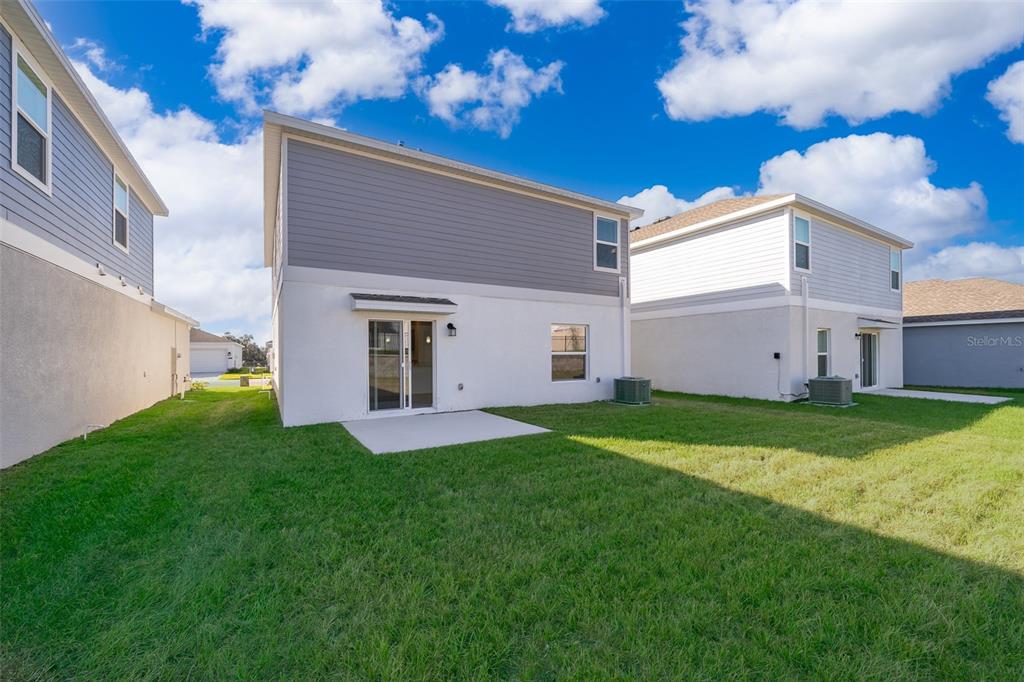 The rear exterior of a two-story house features a small concrete patio and grassy yard — 2723 GENTLE RAIN DRIVE, DAVENPORT, FL