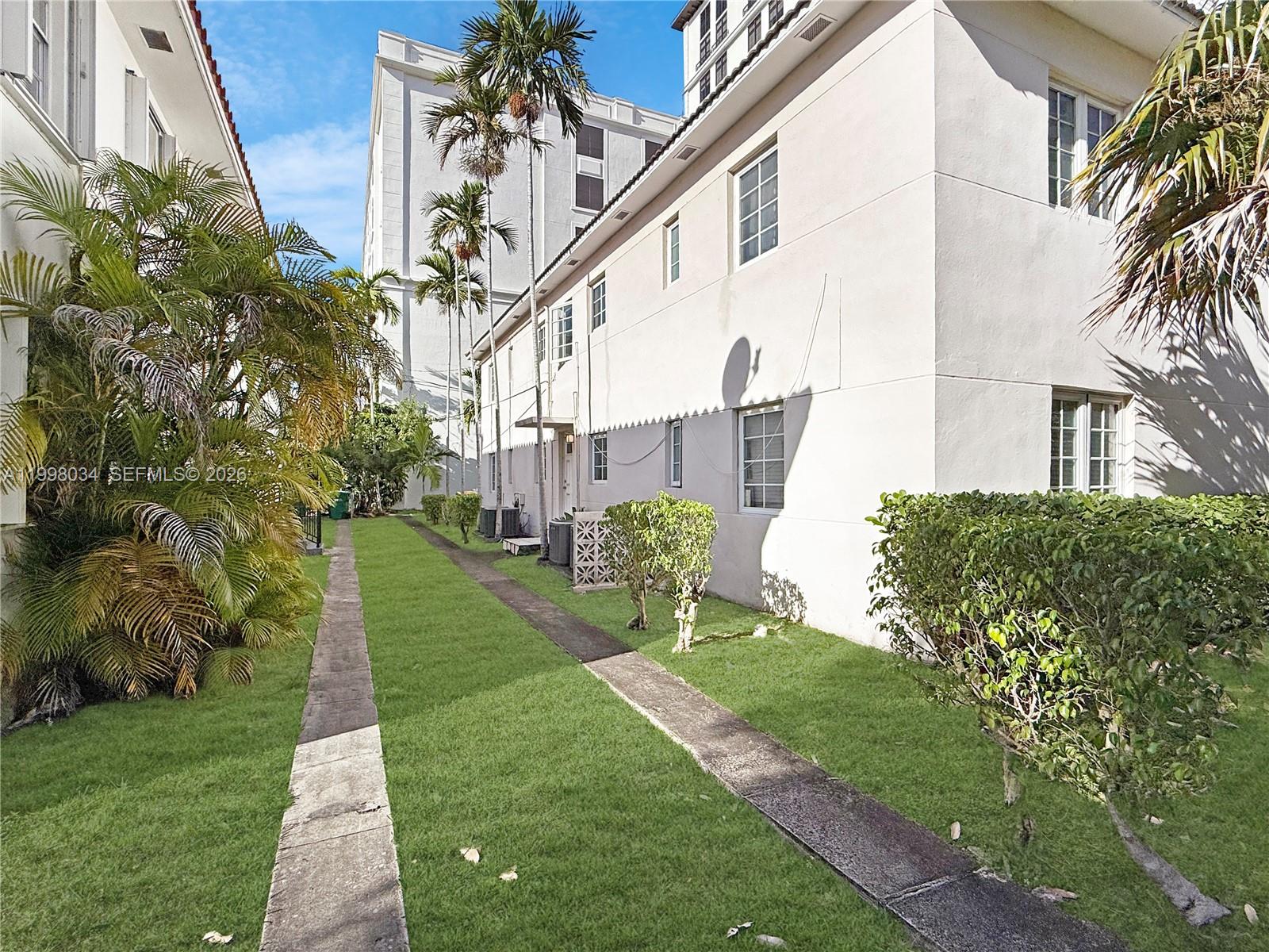 A narrow grassy walkway runs between a two-story building and lush palm trees — 215 Sidonia Ave, Coral Gables FL 33134, CORAL GABLES, FL