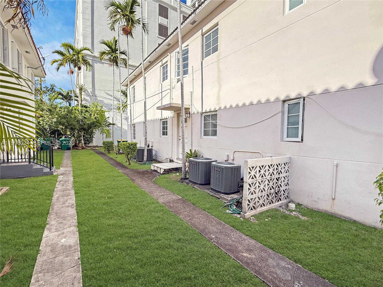 A side view of a multi-story building with a lawn, walkway, and outdoor air conditioning units — 215 Sidonia Ave, Coral Gables FL 33134, CORAL GABLES, FL
