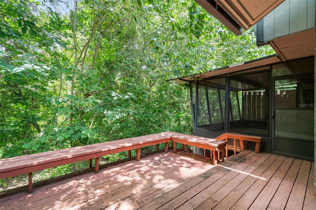 A wooden deck with built-in bench seating overlooks a wooded area next to a screened porch — 1653 NW 19TH CIRCLE, GAINESVILLE, FL