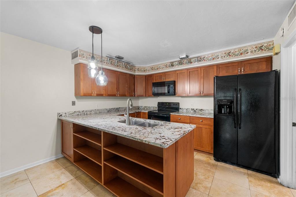 A kitchen with wood cabinets, granite countertops, an island with shelving, and black appliances — 1653 NW 19TH CIRCLE, GAINESVILLE, FL