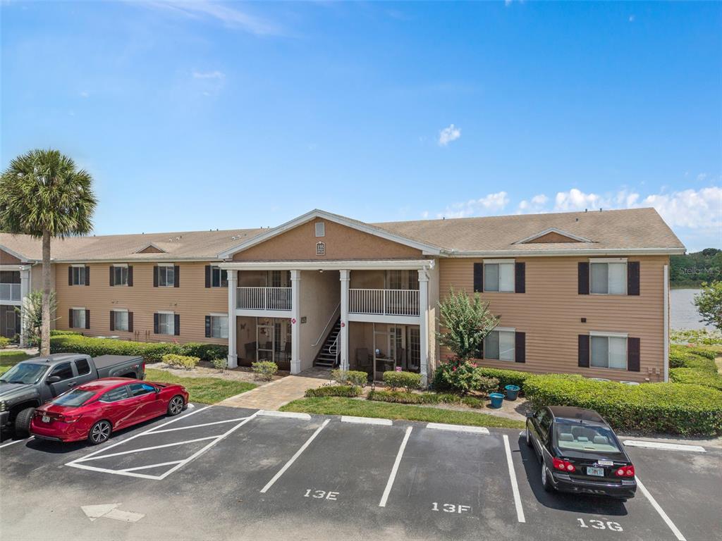 A two-story apartment building with tan siding and a parking lot in the foreground — 155 N PEARL LAKE CAUSEWAY UNIT 208, ALTAMONTE SPRINGS, FL