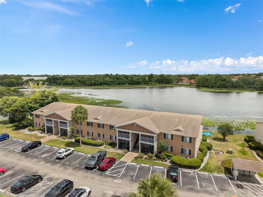 An aerial view shows a multi-story apartment building situated next to a large lake — 155 N PEARL LAKE CAUSEWAY UNIT 208, ALTAMONTE SPRINGS, FL