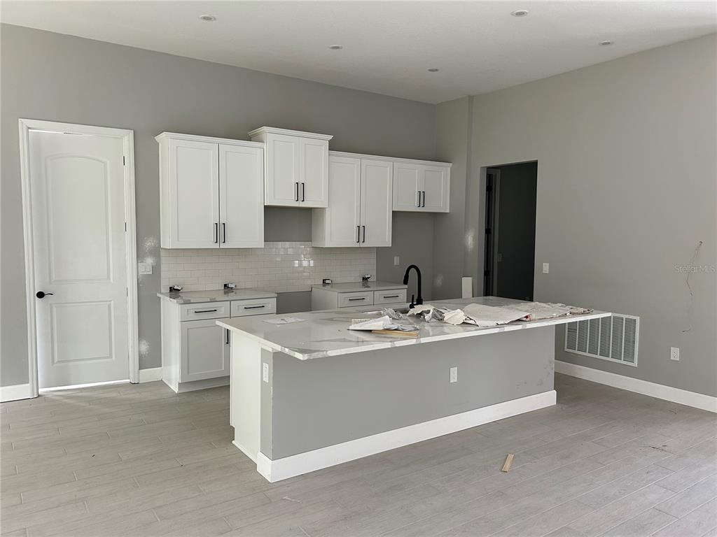 A modern kitchen features white cabinets, a marble-topped island, and light gray tile flooring — 8393 CHRISTOPHER LANE, BROOKSVILLE, FL