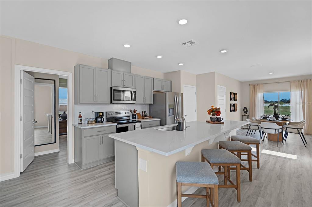 A modern kitchen features gray cabinets, a large quartz island, and stainless steel appliances — 1738 HUMMINGBIRD ROAD, WINTER HAVEN, FL