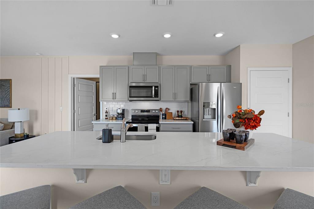A kitchen features a large white quartz island, gray cabinets, and stainless steel appliances — 1738 HUMMINGBIRD ROAD, WINTER HAVEN, FL