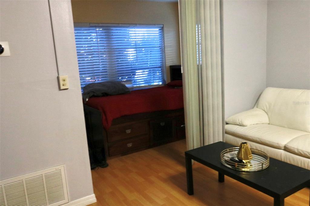 A living area with a white sofa and a partitioned bedroom featuring a wooden bed — 3125 36TH STREET N UNIT 103, ST PETERSBURG, FL