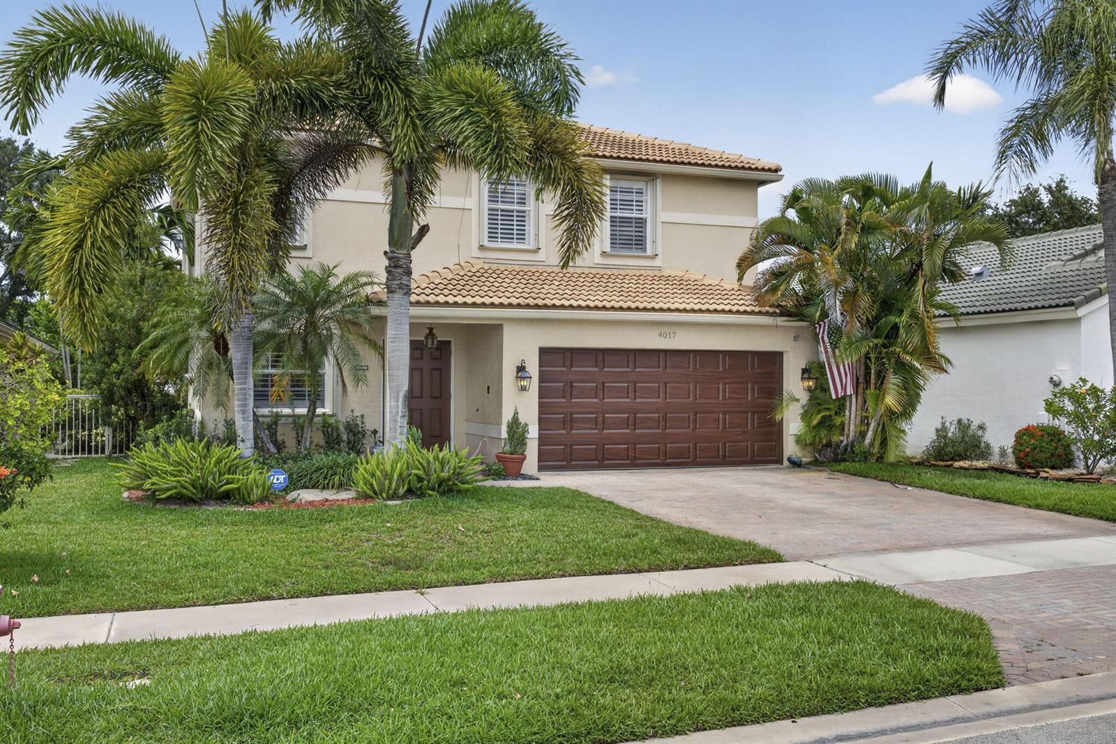 A two-story house with a tan stucco exterior, a brown garage door, and palm trees — 4017 Bluff Harbor Way, Wellington FL 33449, WELLINGTON, FL